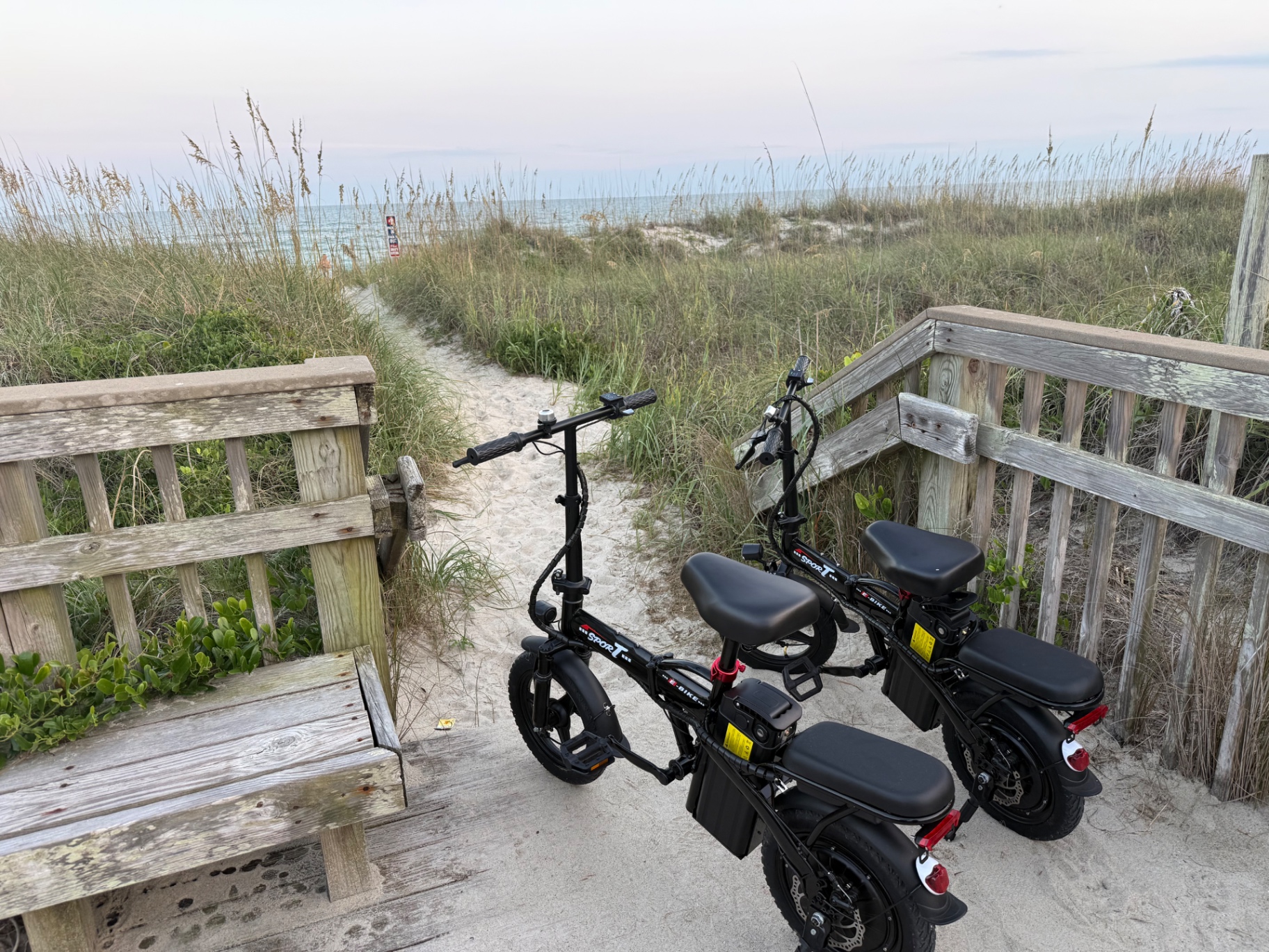 Two EVRYDAY Go folding electric bikes on a beach boardwalk with the ocean in the background