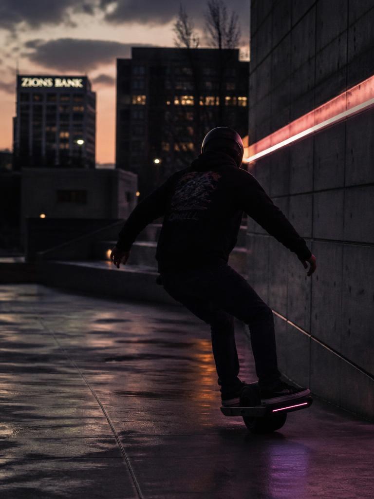 Rider carving a onewheel electric board in a concrete plaza at dusk